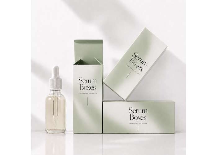 Glass serum dropper bottle displayed beside three soft green and white serum packaging boxes on a clean white background.